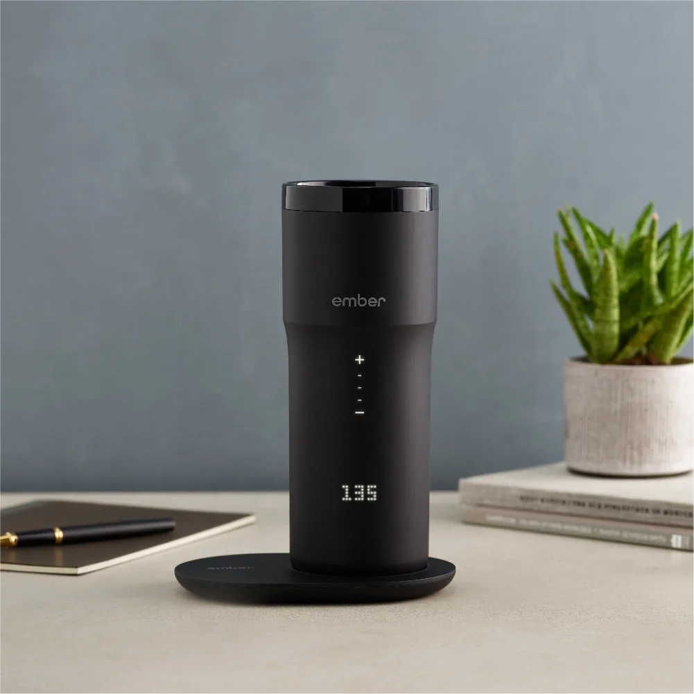 Ember Travel Mug 2 on a desk beside a notebook and plant