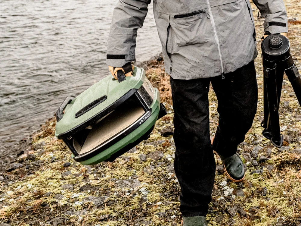 Person carrying the Gozney Tread Portable Pizza Oven by the water